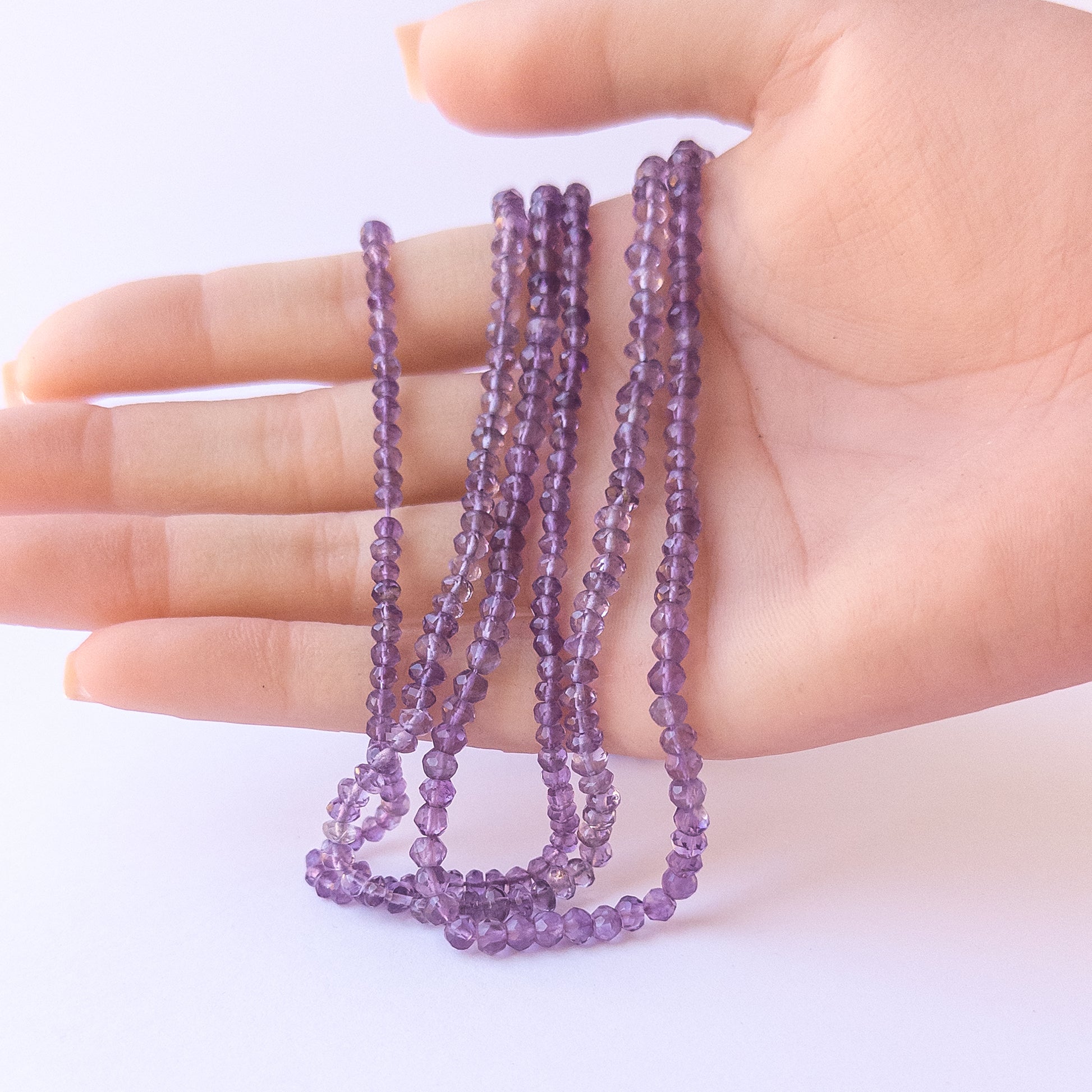 A person holds delicate strands of Amethyst beads, showcasing their faceted rondelle design.
