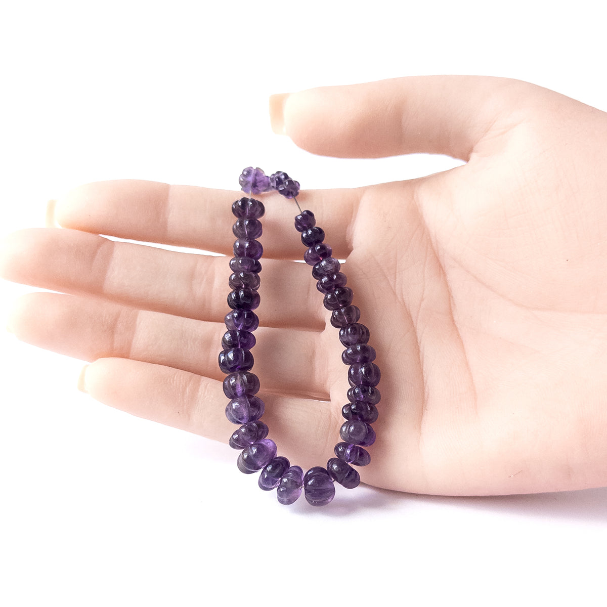 A person holds delicate pieces of Amethyst beads, showcasing their pumpkin cut design.