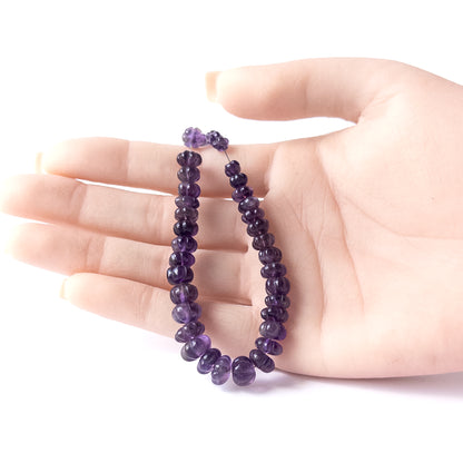 A person holds delicate pieces of Amethyst beads, showcasing their pumpkin cut design.