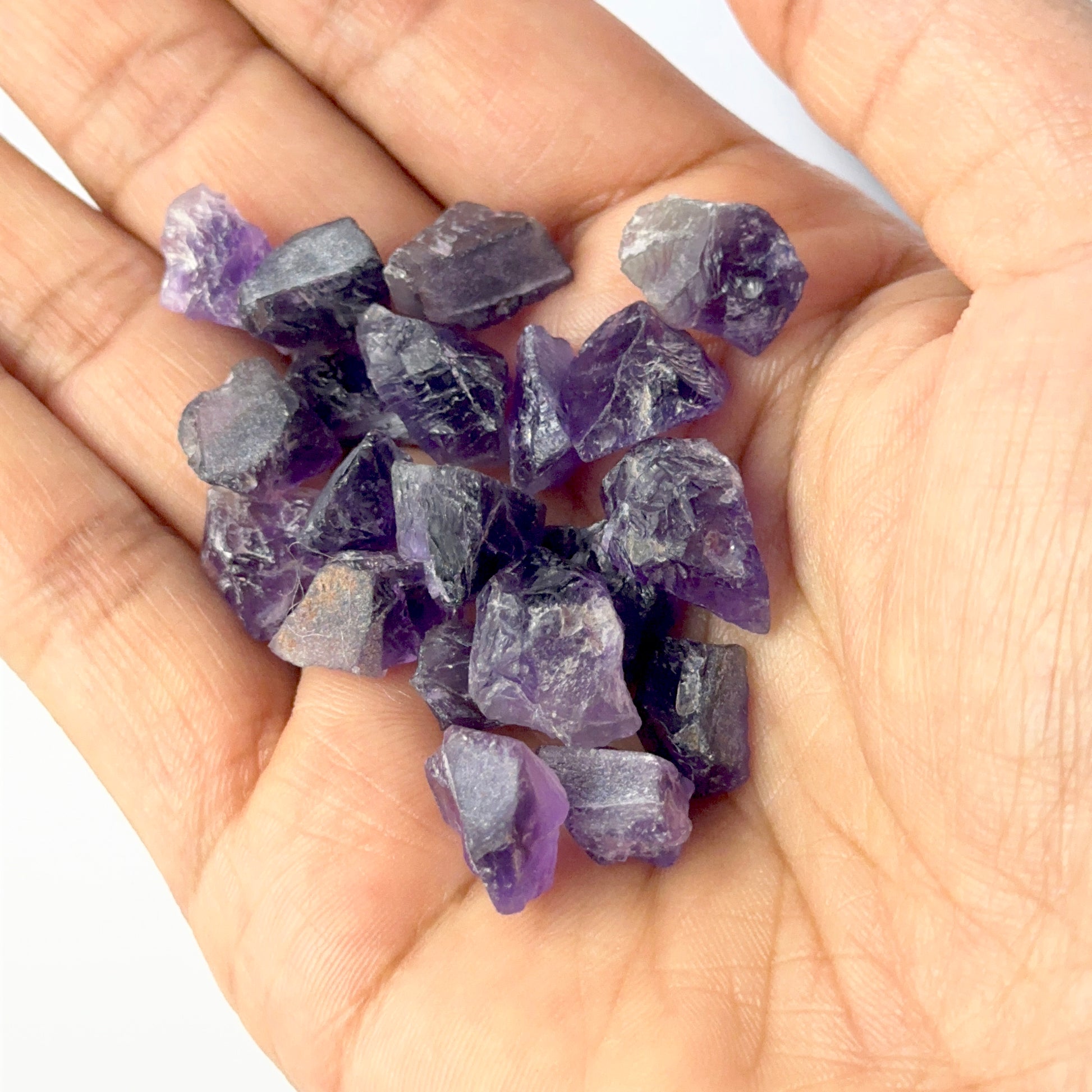 A person holds delicate pieces of Amethyst rough, showcasing their natural rough design.