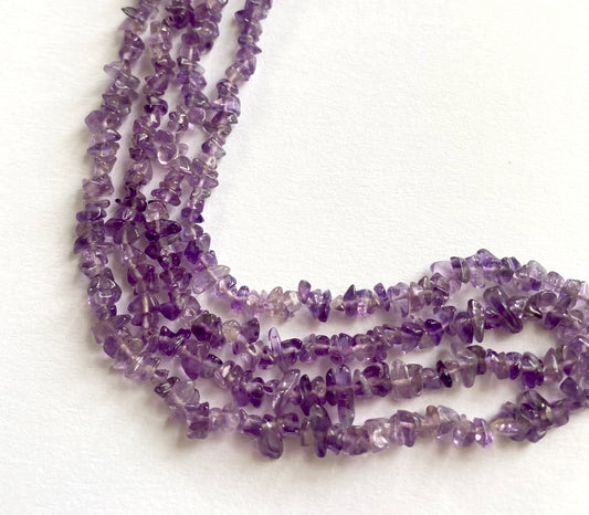 Amethyst smooth chip beads with mixed purple hues laid out in a natural curve on fabric.
