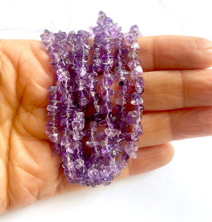 A person holds delicate strands of Amethyst beads, showcasing their smooth design.