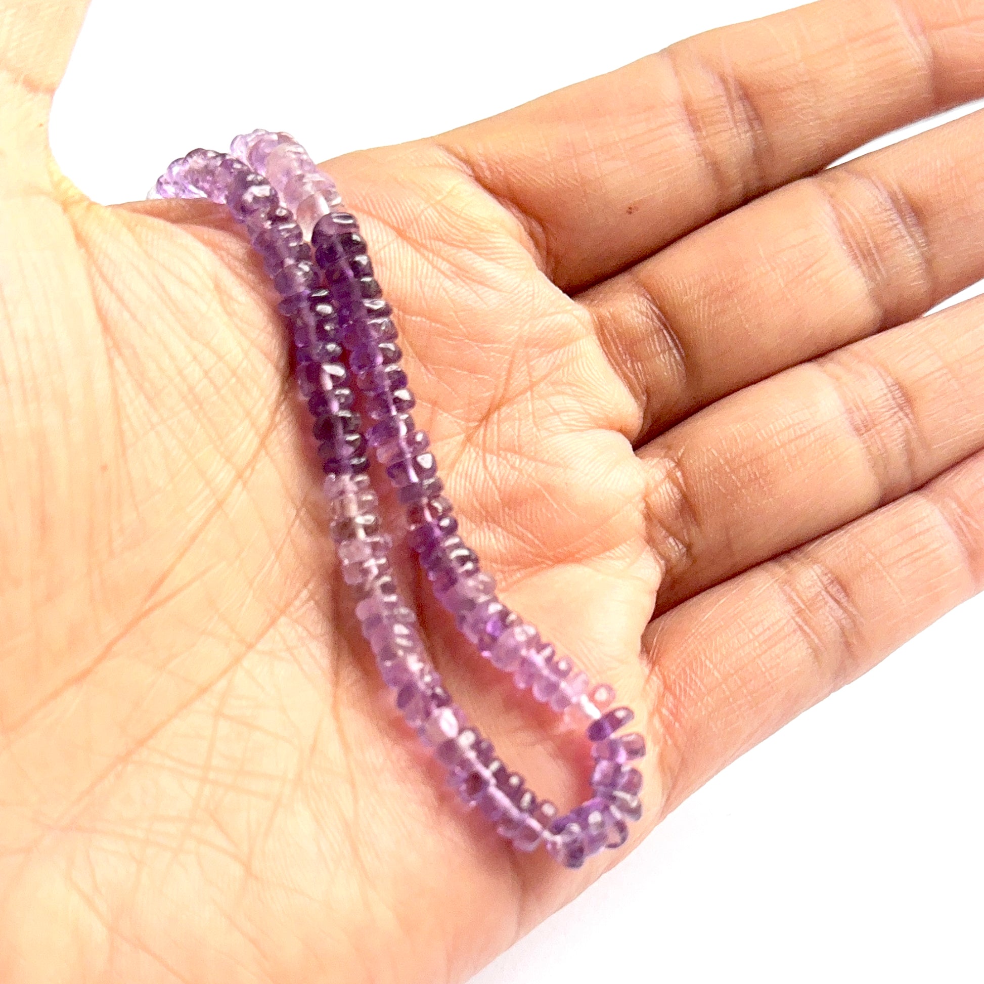 A person holds delicate strands of amethyst heishi beads, showcasing their smooth design.