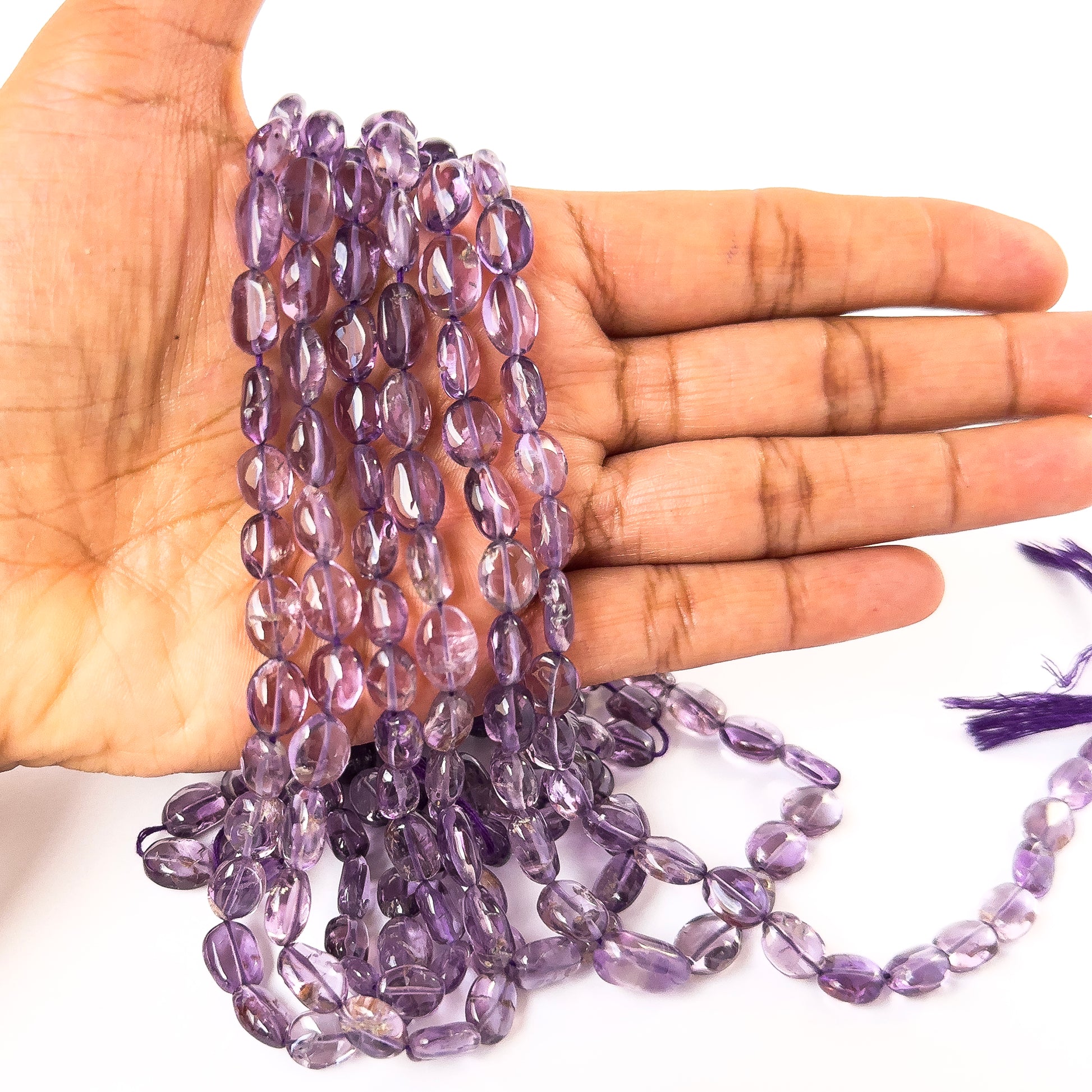 A person holds delicate strands of Amethyst smooth oval beads, showcasing their polished oval design.