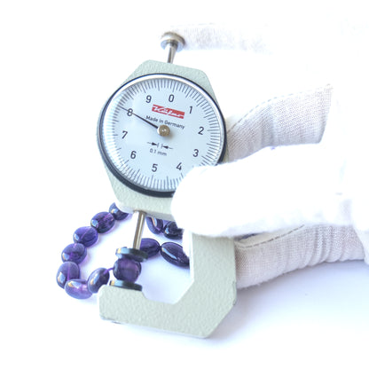 A dial gauge measures the Amethyst smooth oval 8mm gemstone.