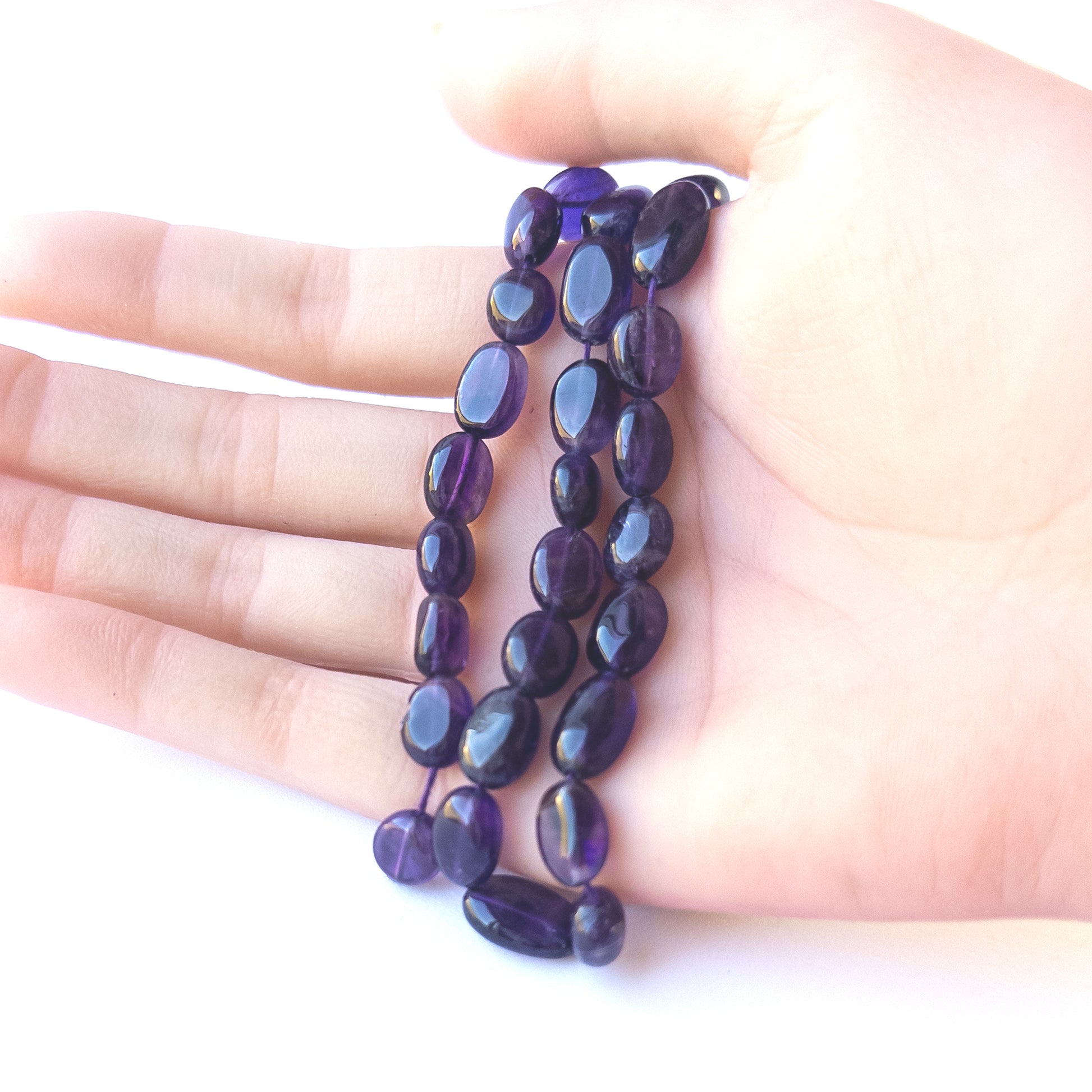 A person holds delicate strands of Amethyst beads, showcasing their smooth oval design.