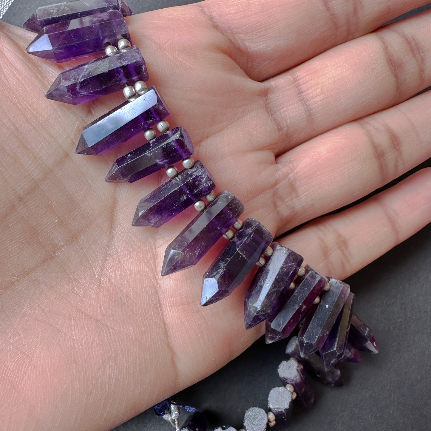 A person holds delicate strands of amethyst beads, showcasing their smooth design.