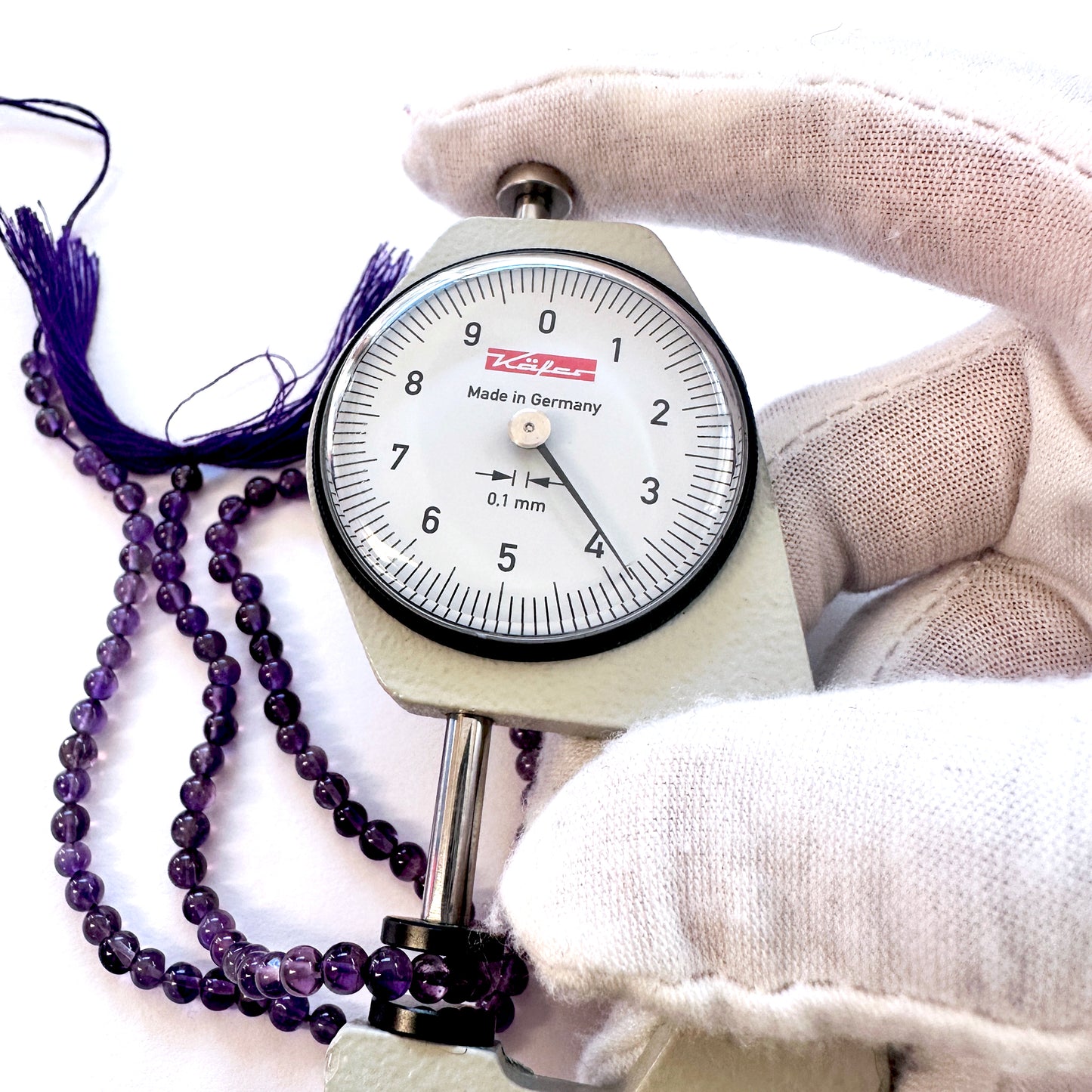 A dial gauge measures the Amethyst smooth round 3.7-3.9mm gemstone.