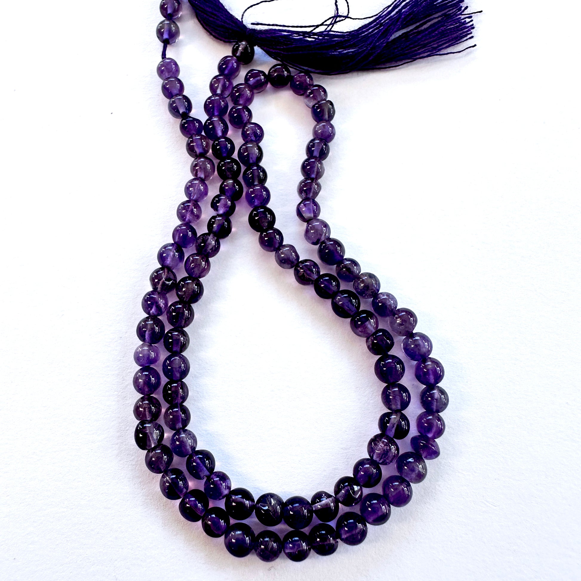 Close-up of Amethyst smooth round beads with deep purple tones and glossy finish.