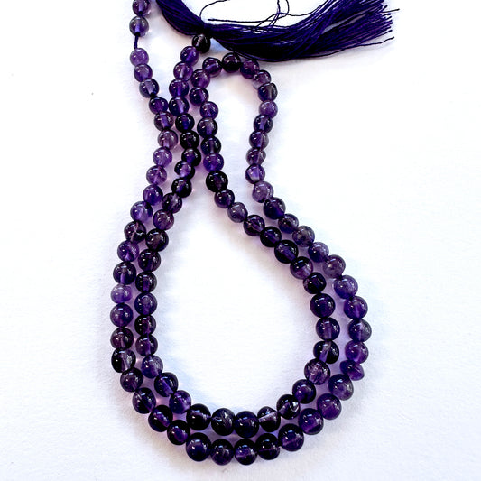 Close-up of Amethyst smooth round beads with deep purple tones and glossy finish.