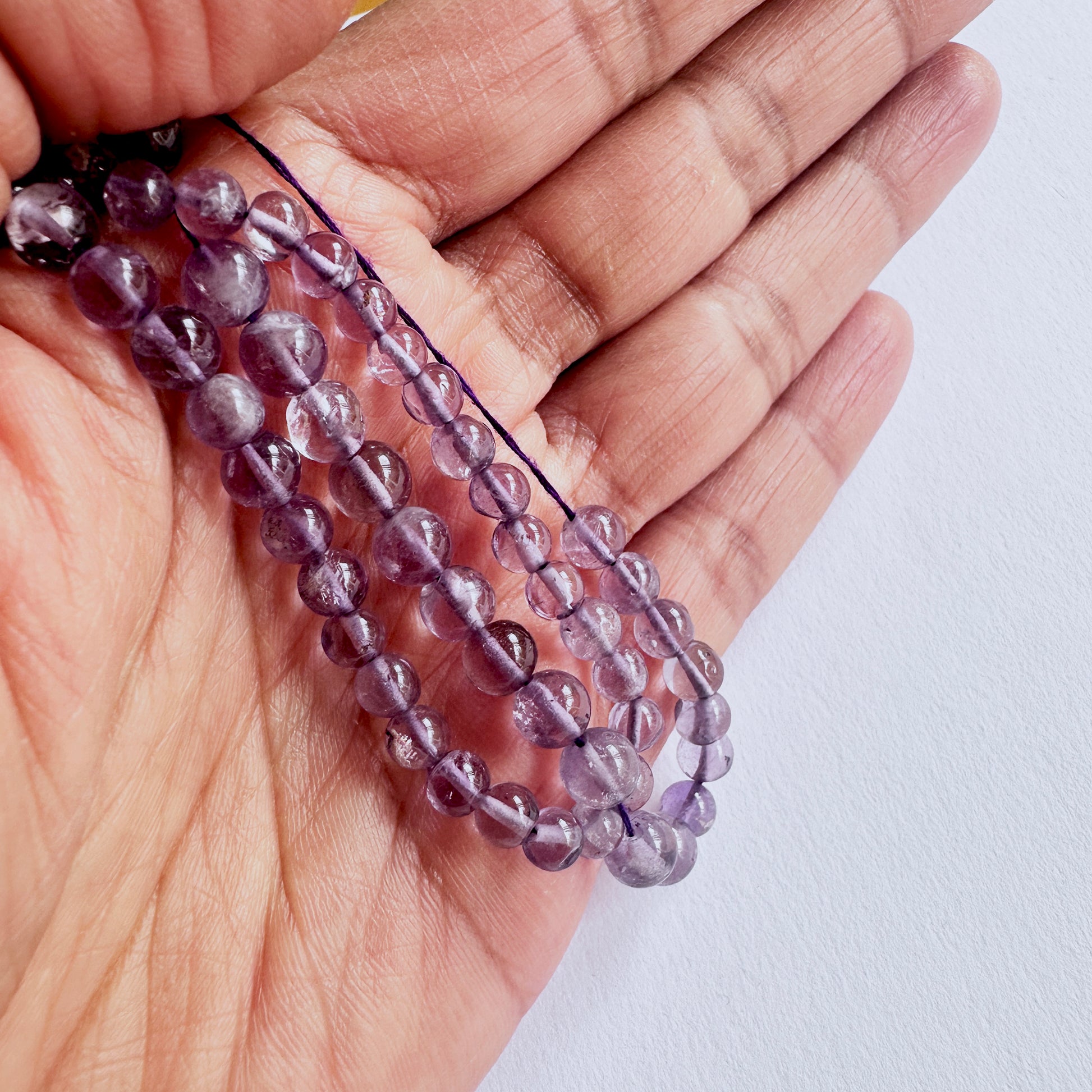 A person holds delicate strands of Amethyst beads, showcasing their smooth design.