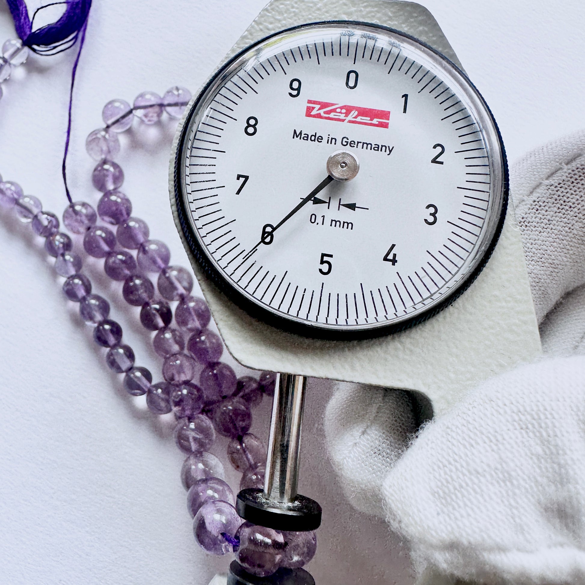 A dial gauge measures the Amethyst smooth round gemstone.