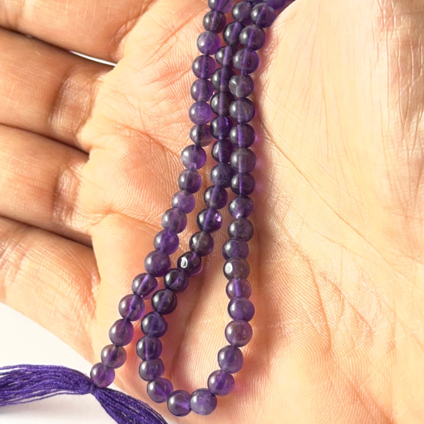 A person holds delicate strands of Amethyst beads, showcasing their smooth round design.
