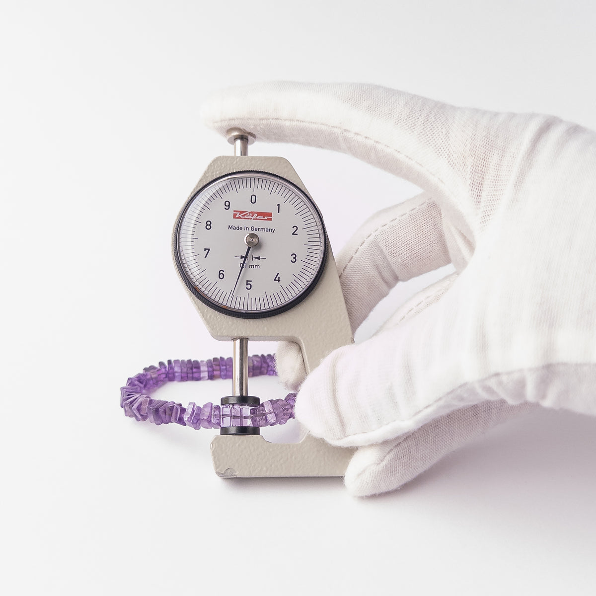 A dial gauge measures the Amethyst Smooth Square Heishi 5.5-6mm gemstone.