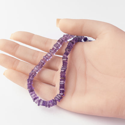 A person holds delicate strands of Amethyst beads, showcasing their smooth square heishi design.