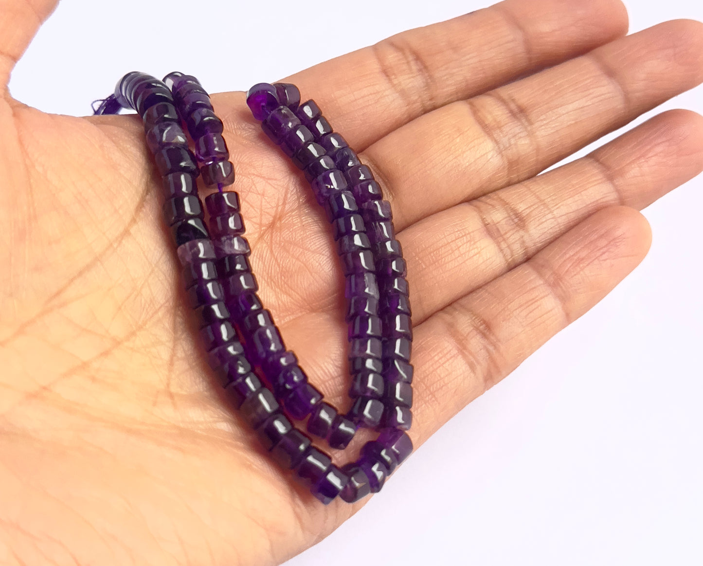 A person holds delicate strands of Amethyst beads, showcasing their smooth design.