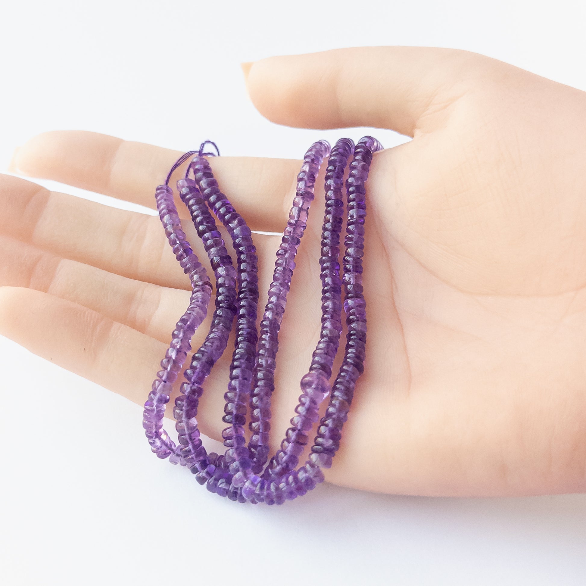 A person holds delicate strands of Amethyst smooth wheel beads, showcasing their polished design.