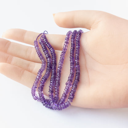A person holds delicate strands of Amethyst smooth wheel beads, showcasing their polished design.
