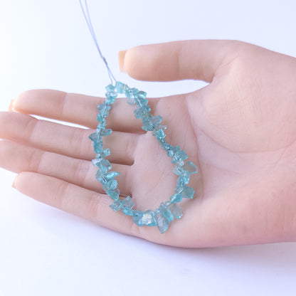 A person holds delicate pieces of Apatite rough beads, showcasing their drilled rough design.