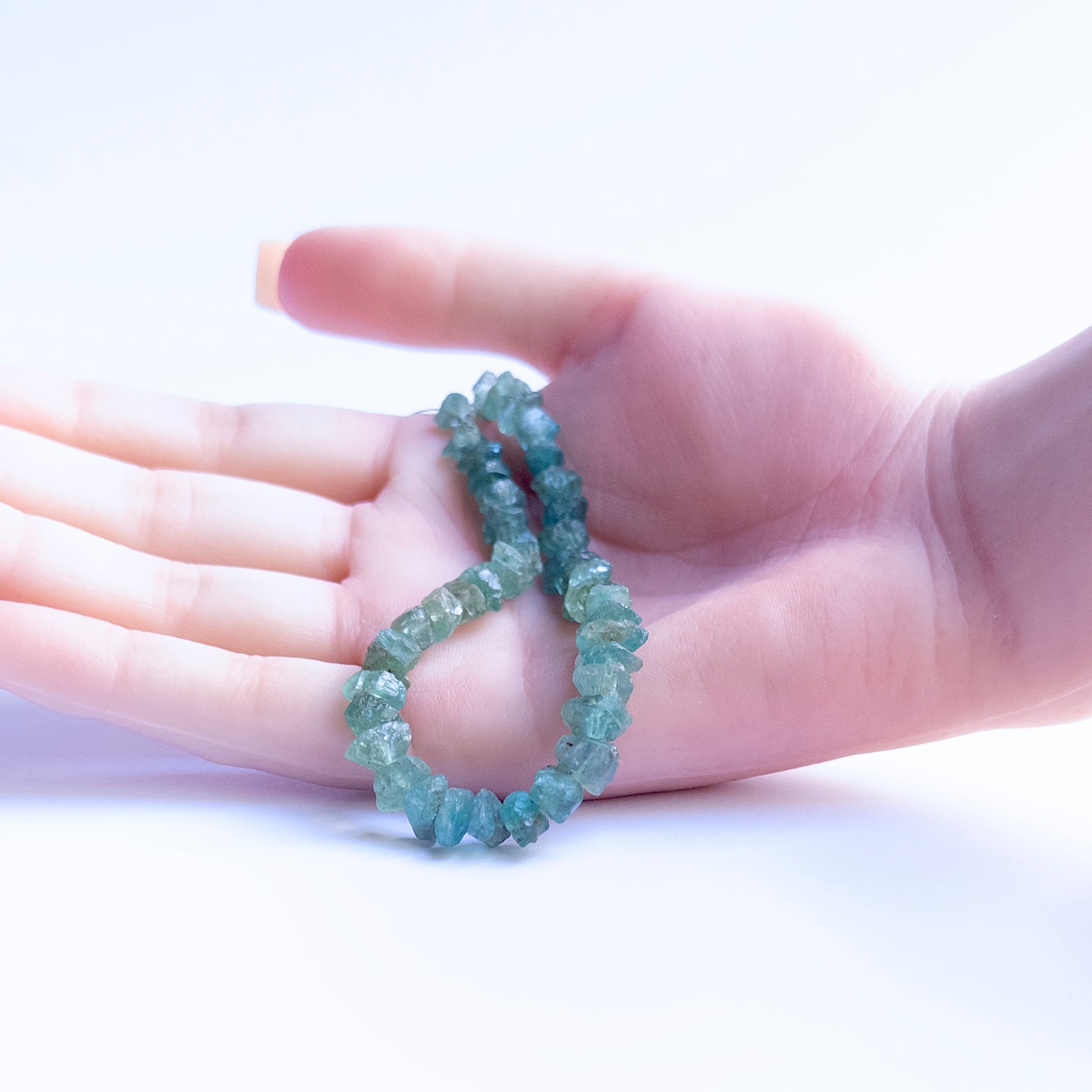 A person holds delicate pieces of Apatite drilled rough beads, showcasing their texture.