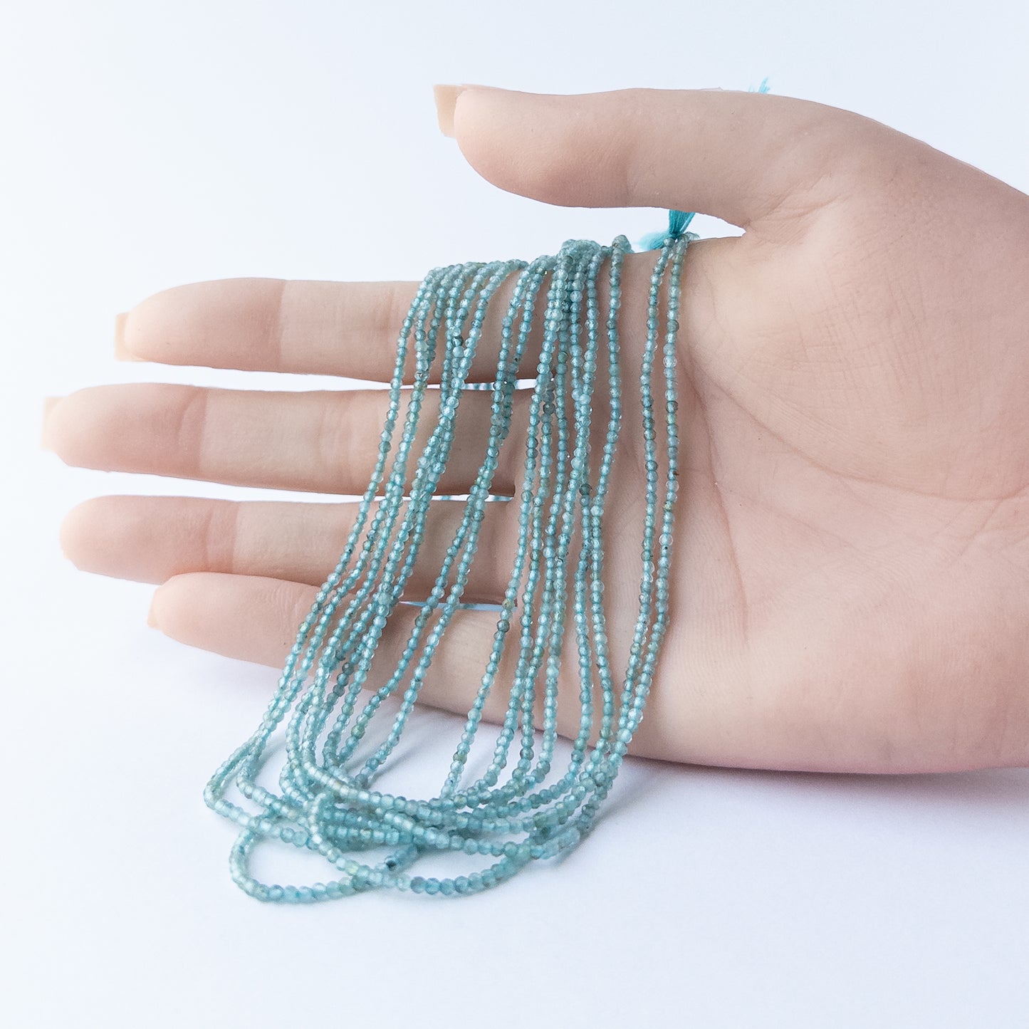A person holds delicate strands of Apatite beads, showcasing their faceted rondelle design.