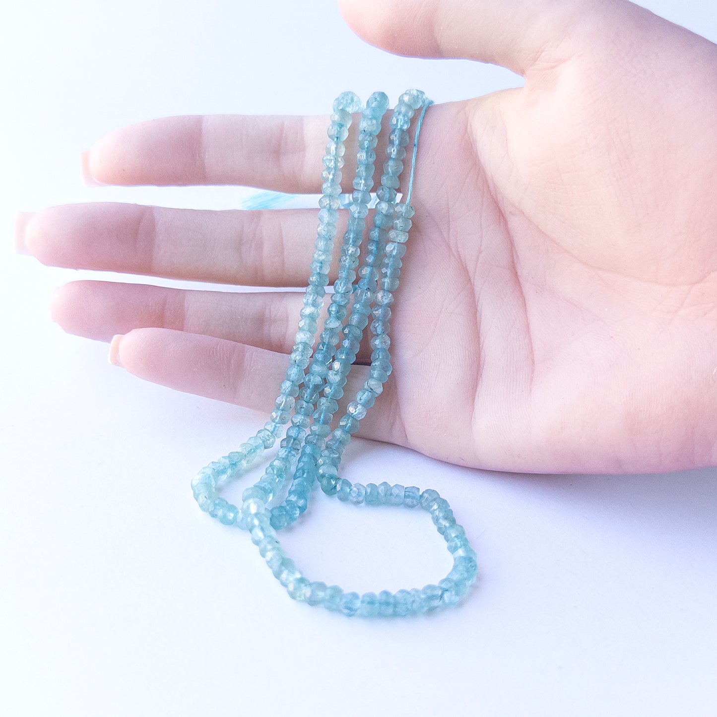 A person holds delicate strands of Apatite beads, showcasing their faceted rondelle design.