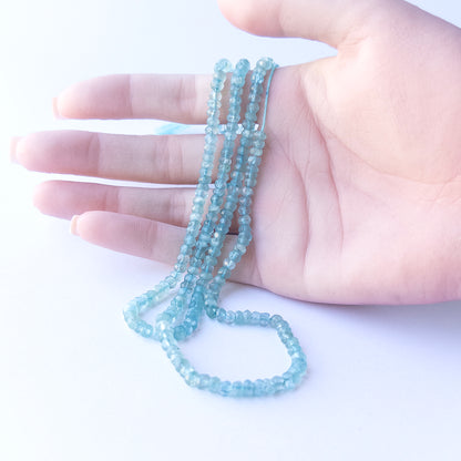 A person holds delicate strands of Apatite beads, showcasing their faceted rondelle design.