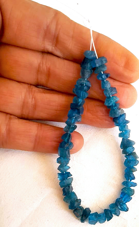 A person holds delicate strands of Apatite beads, showcasing their natural design.