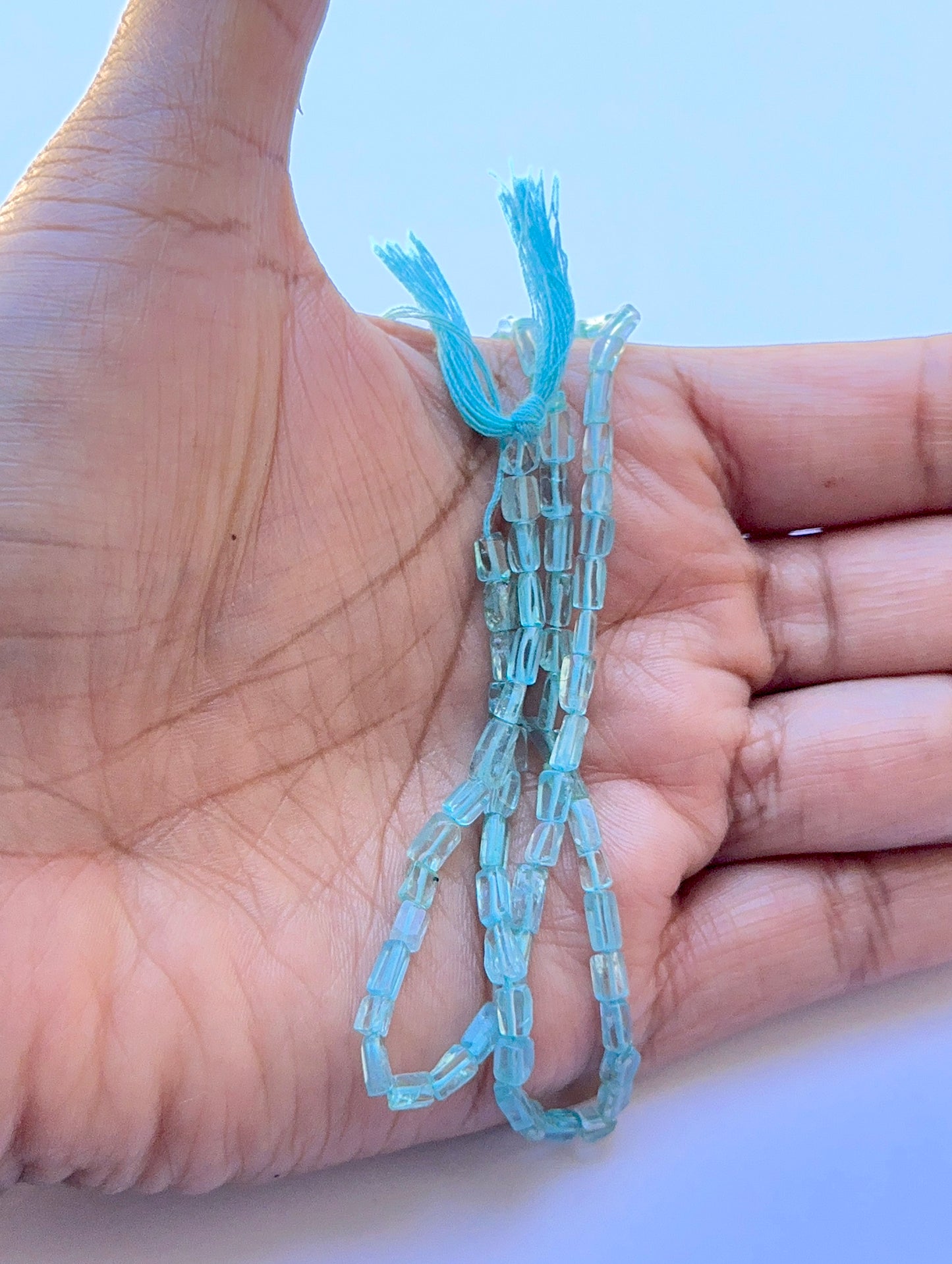 A person holds delicate strands of Apatite beads, showcasing their smooth design.