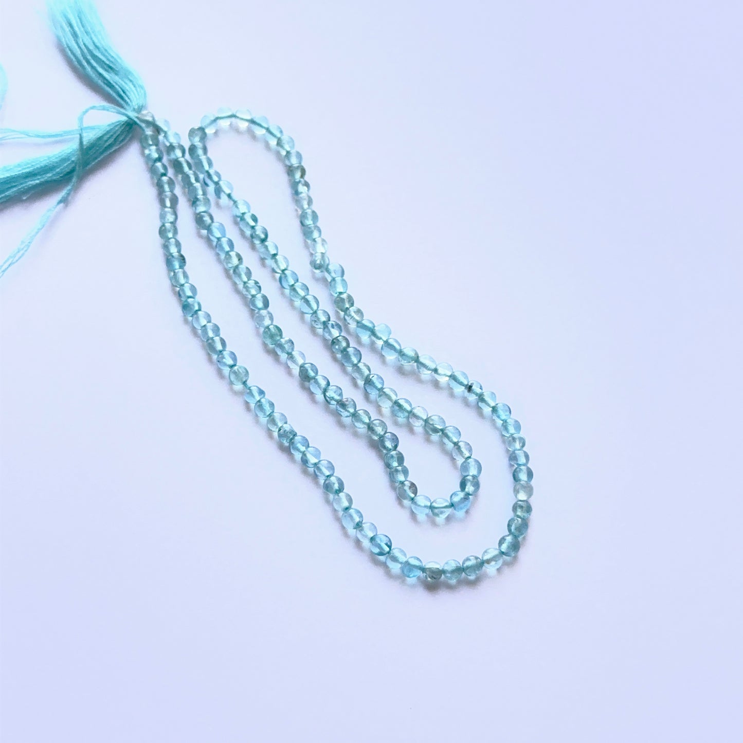 Apatite smooth round natural gemstone beads in bright blue tones arranged on a 34cm strand for handmade jewellery components.