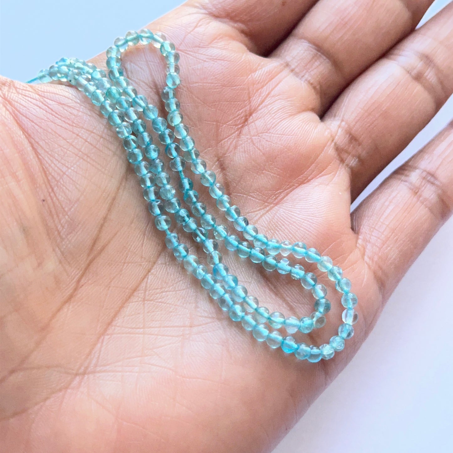 A person holds delicate strands of Apatite beads, showcasing their smooth design.