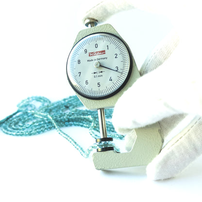 A dial gauge measures the Apatite Smooth Round 3.4–3.6mm gemstone.