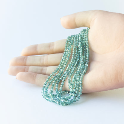 A person holds delicate strands of Apatite beads, showcasing their Smooth Round design.