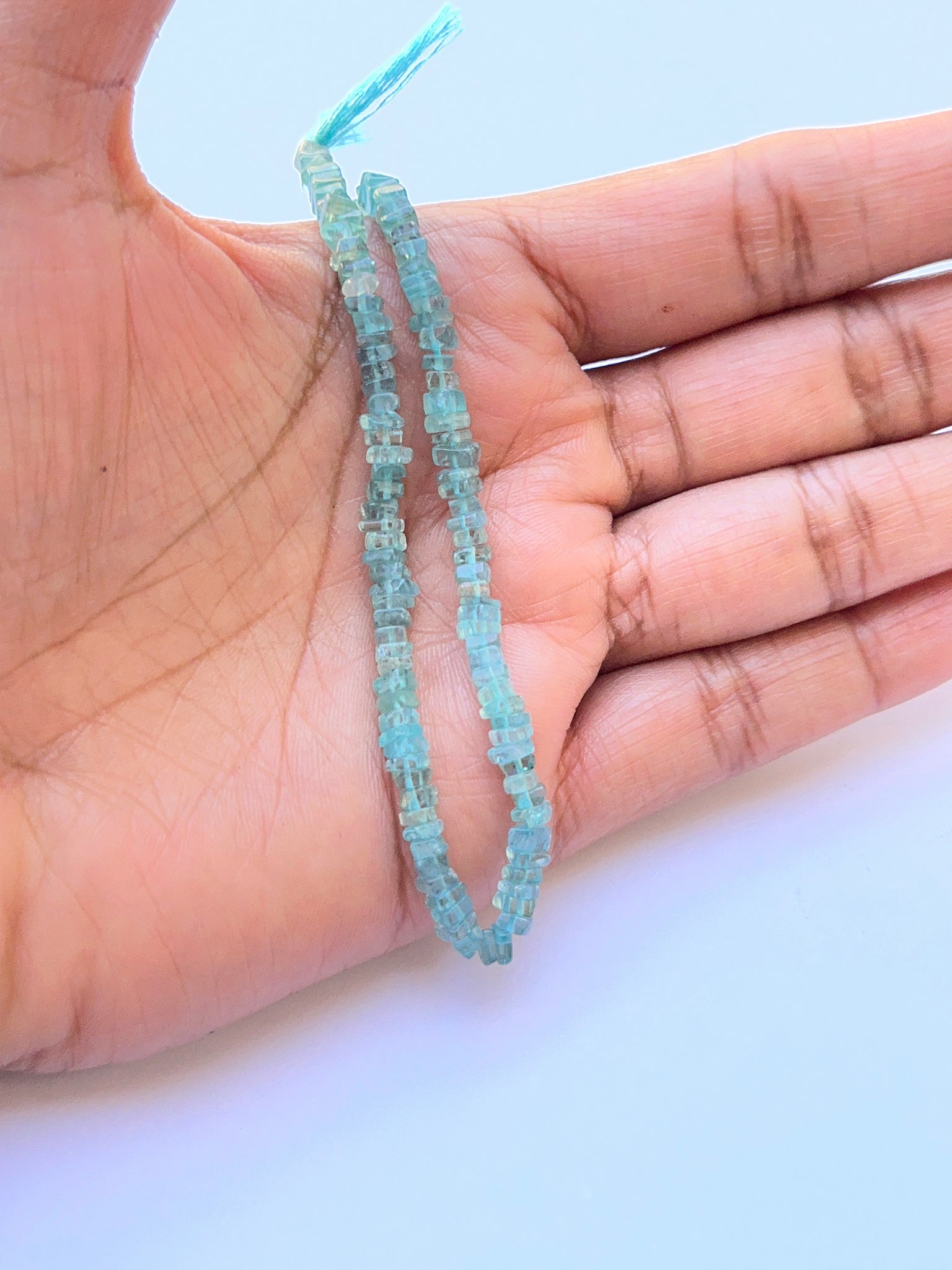 A person holds delicate strands of Apatite beads, showcasing their smooth design.