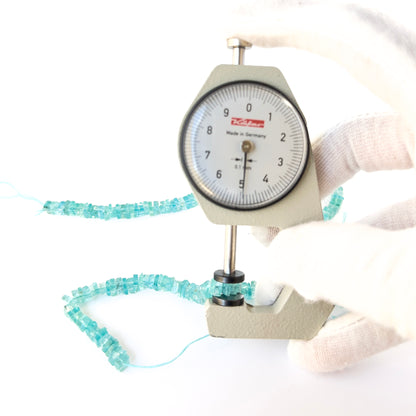A dial gauge measures the Apatite smooth square heishi 4.5–5mm gemstone.