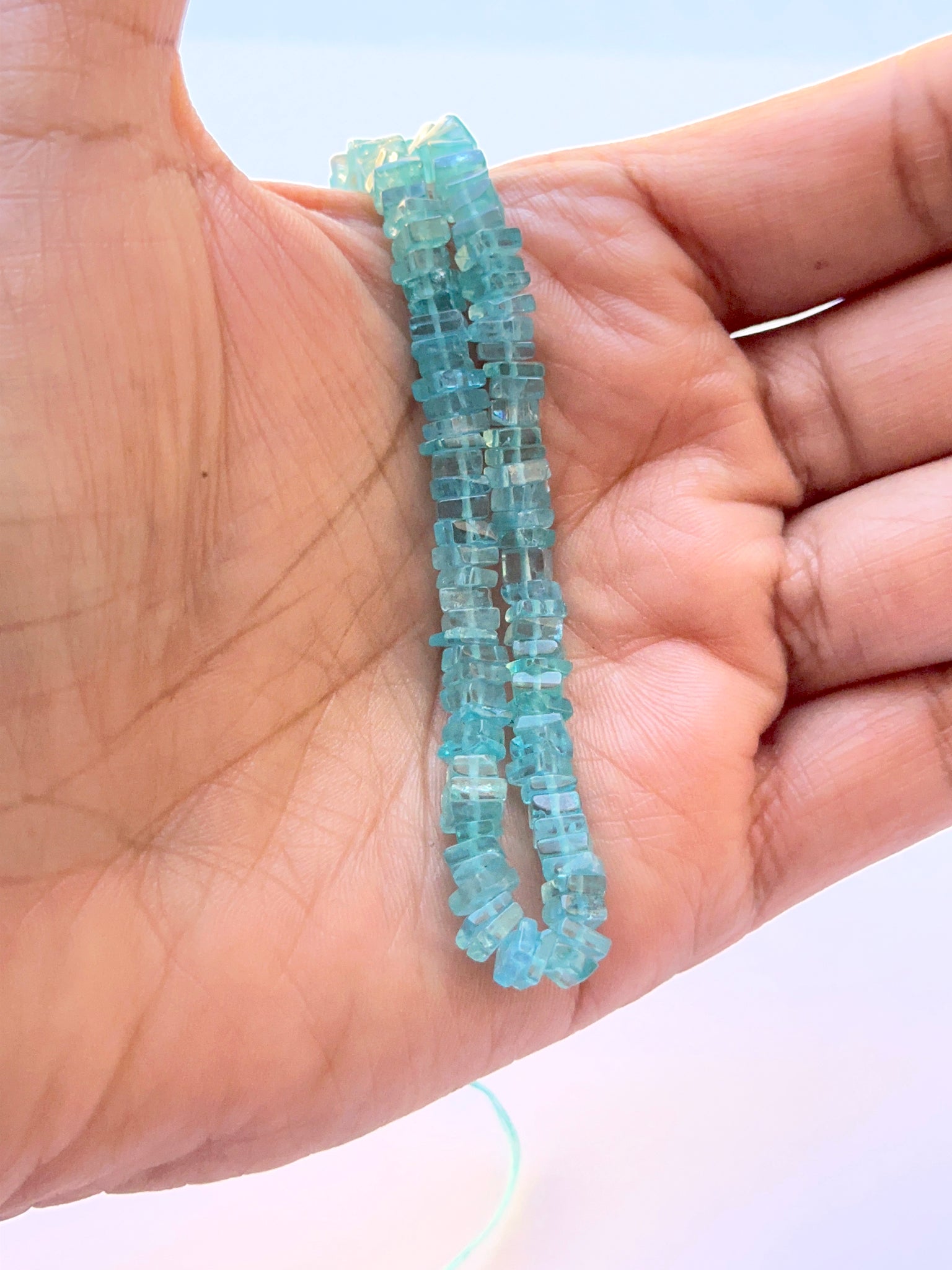 A person holds delicate strands of Apatite beads, showcasing their smooth design.