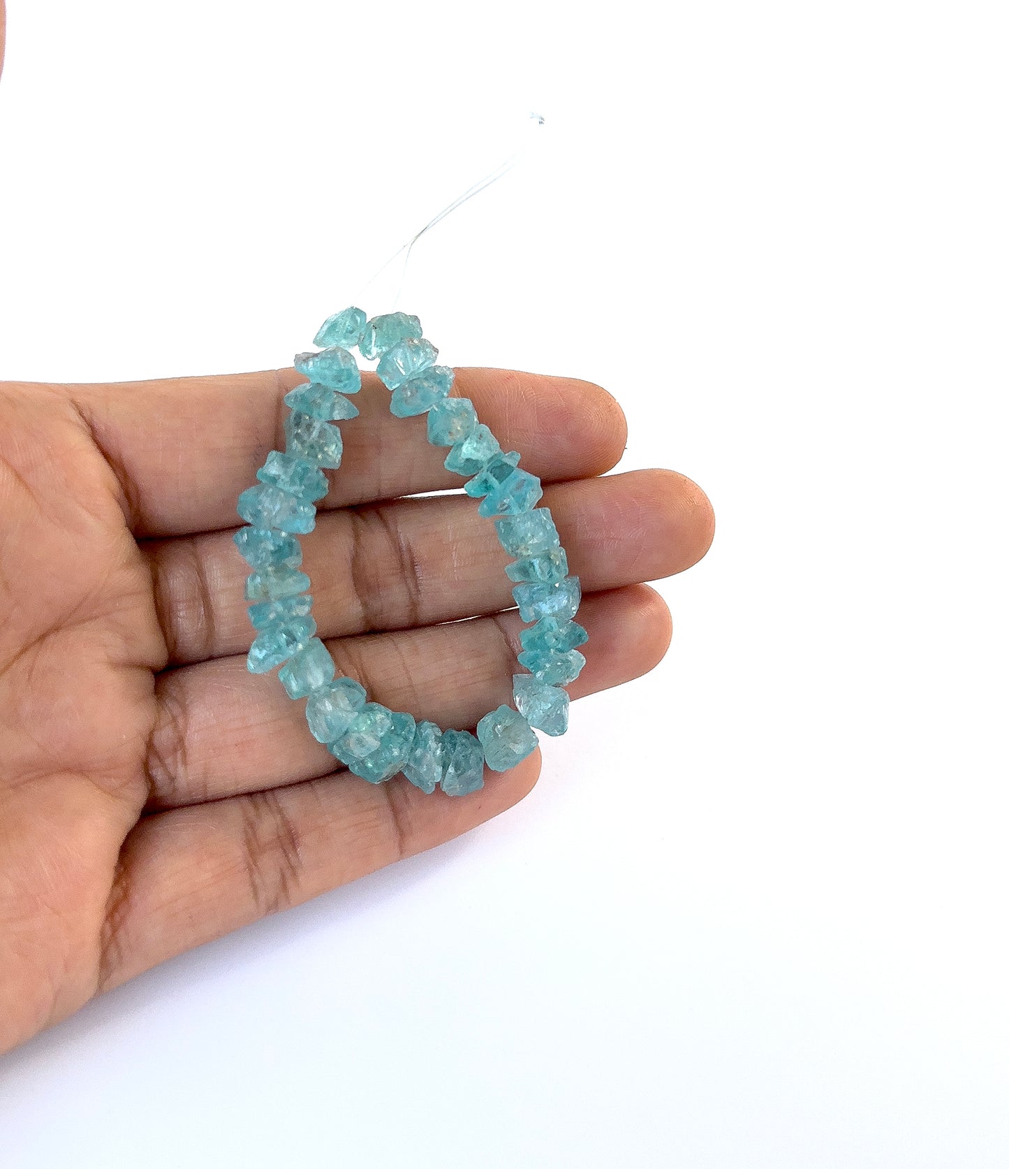 A person holds delicate pieces of Apatite undrilled rough, showcasing their natural raw design.