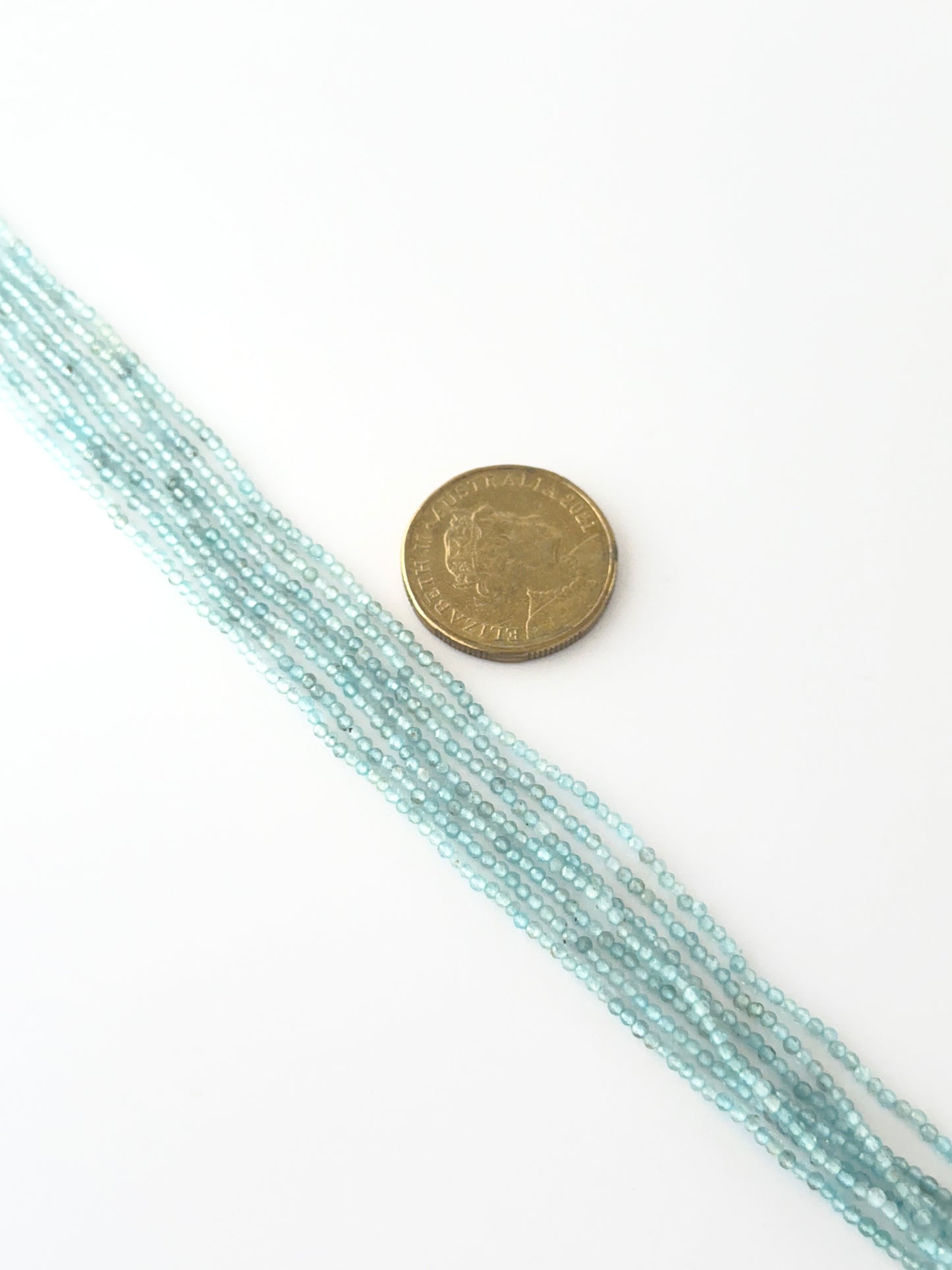 A coin is placed near delicate strands of Aquamarine beads for scale