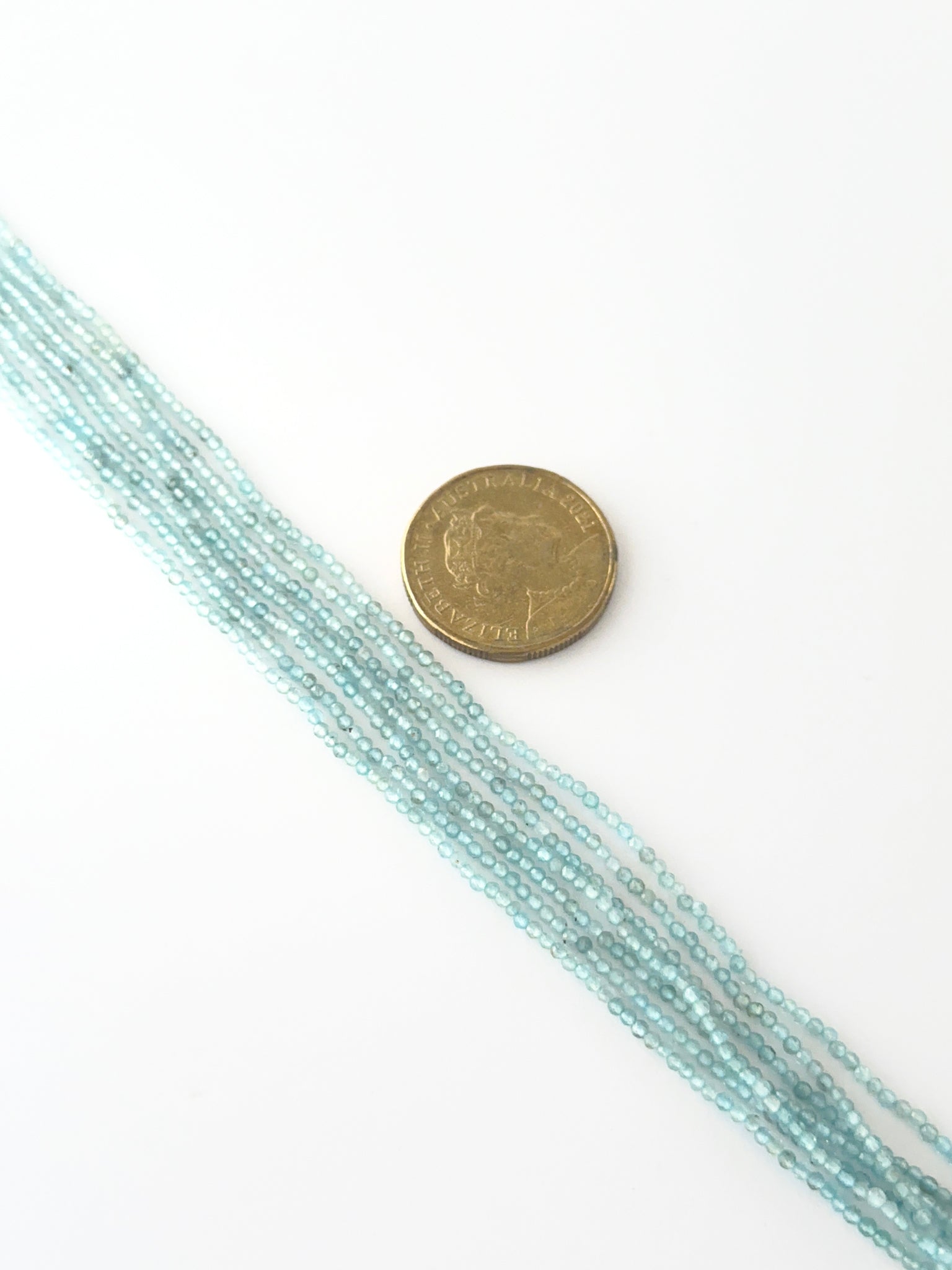 A coin is placed near delicate strands of Aquamarine beads for scale