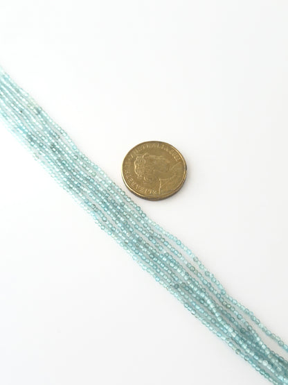 A coin is placed near delicate strands of Aquamarine beads for scale