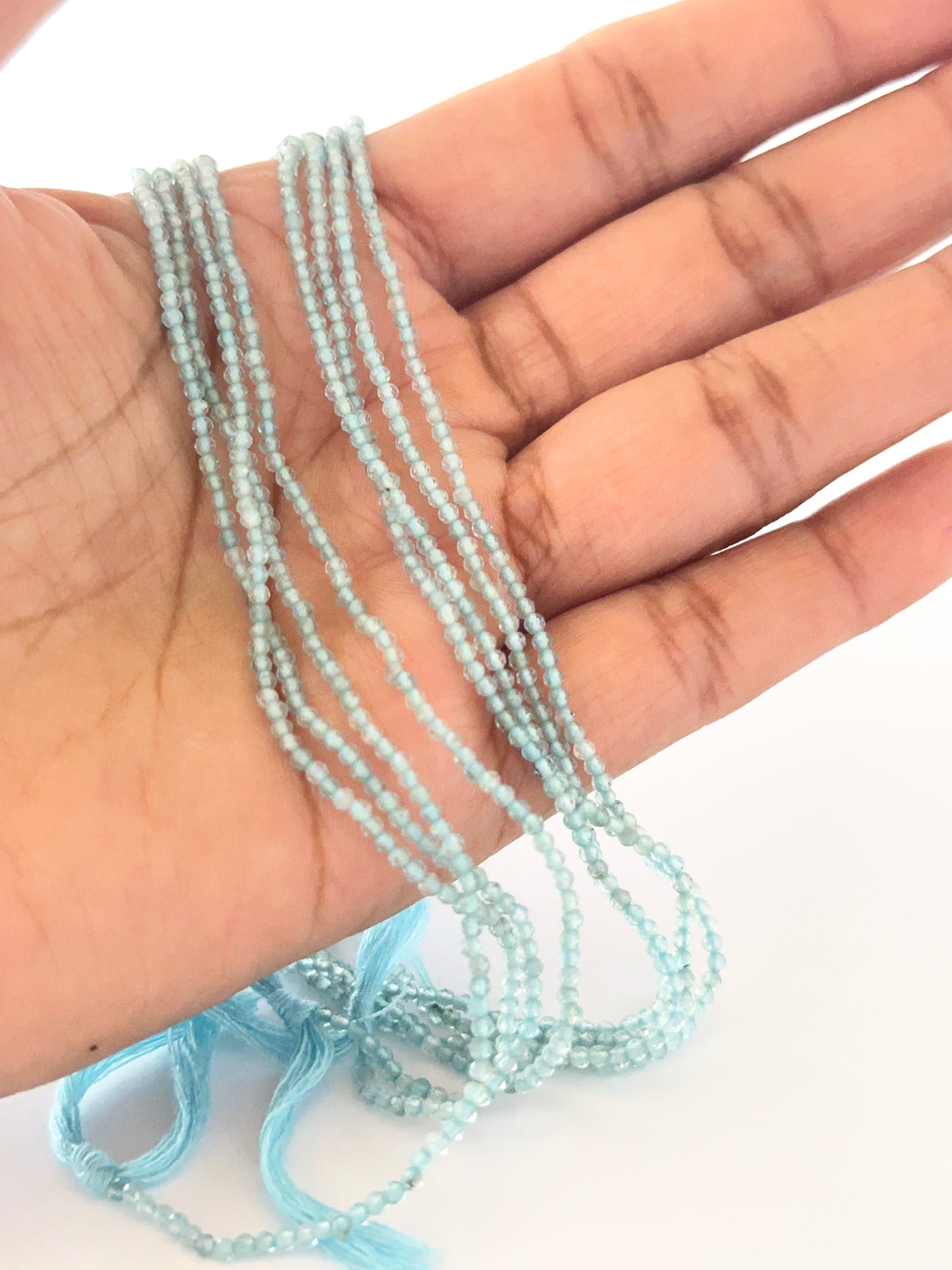 A person holds delicate strands of Aquamarine beads, showcasing their faceted rondelle design.