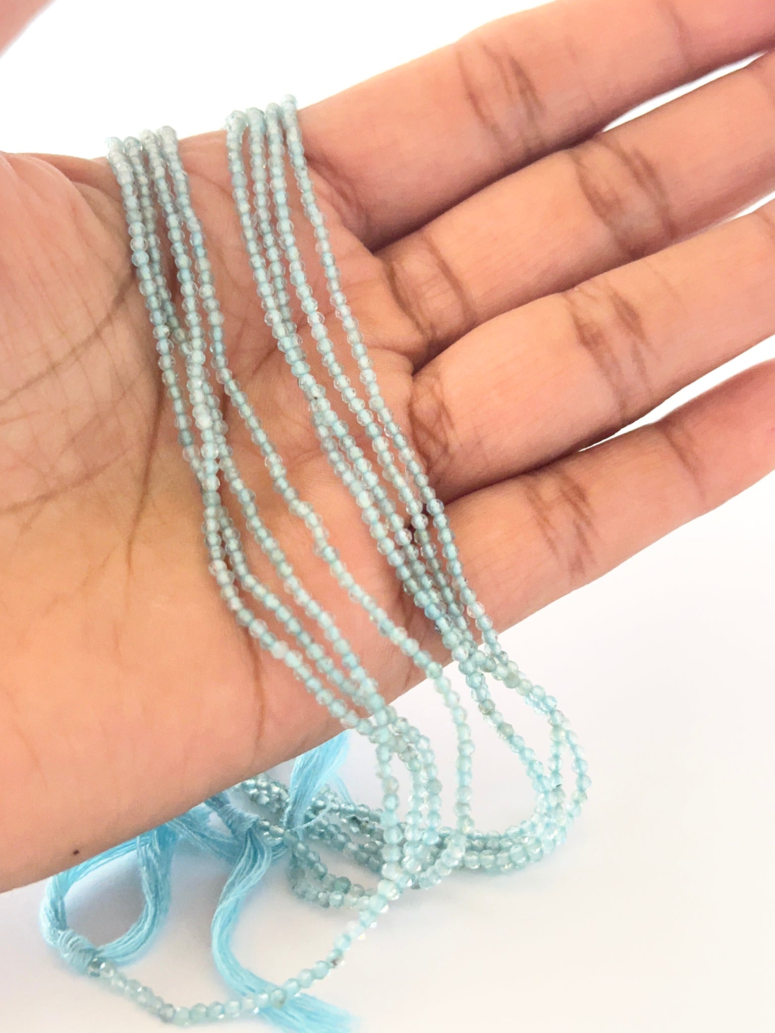 A person holds delicate strands of Aquamarine beads, showcasing their faceted rondelle design.