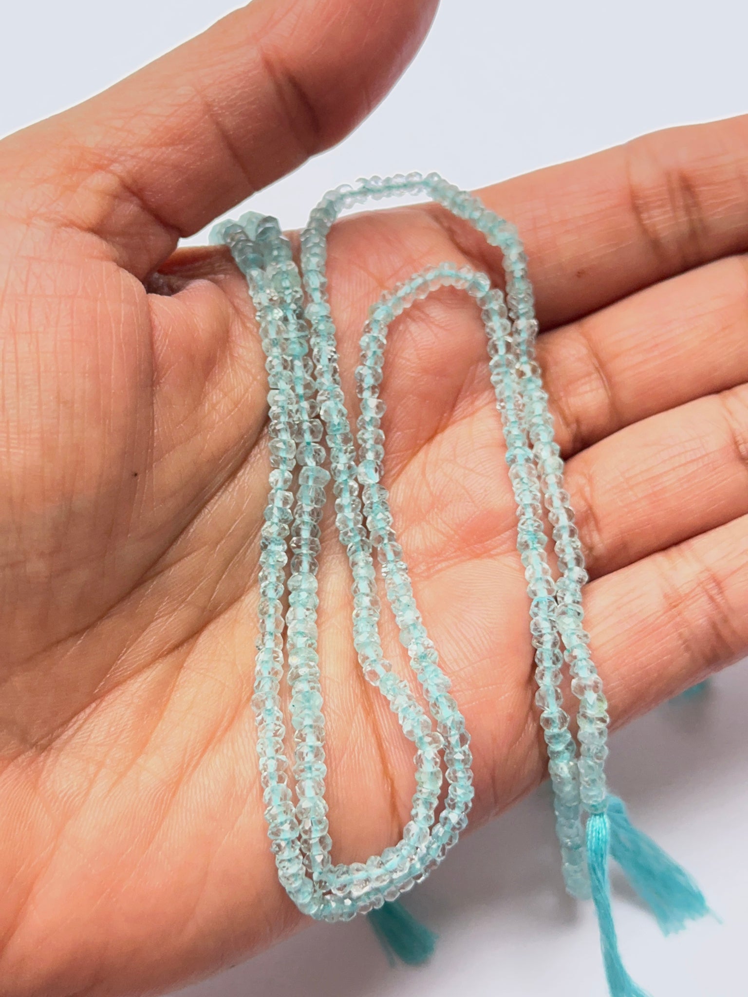 A person holds delicate strands of Lavender Opal beads, showcasing their smooth design.