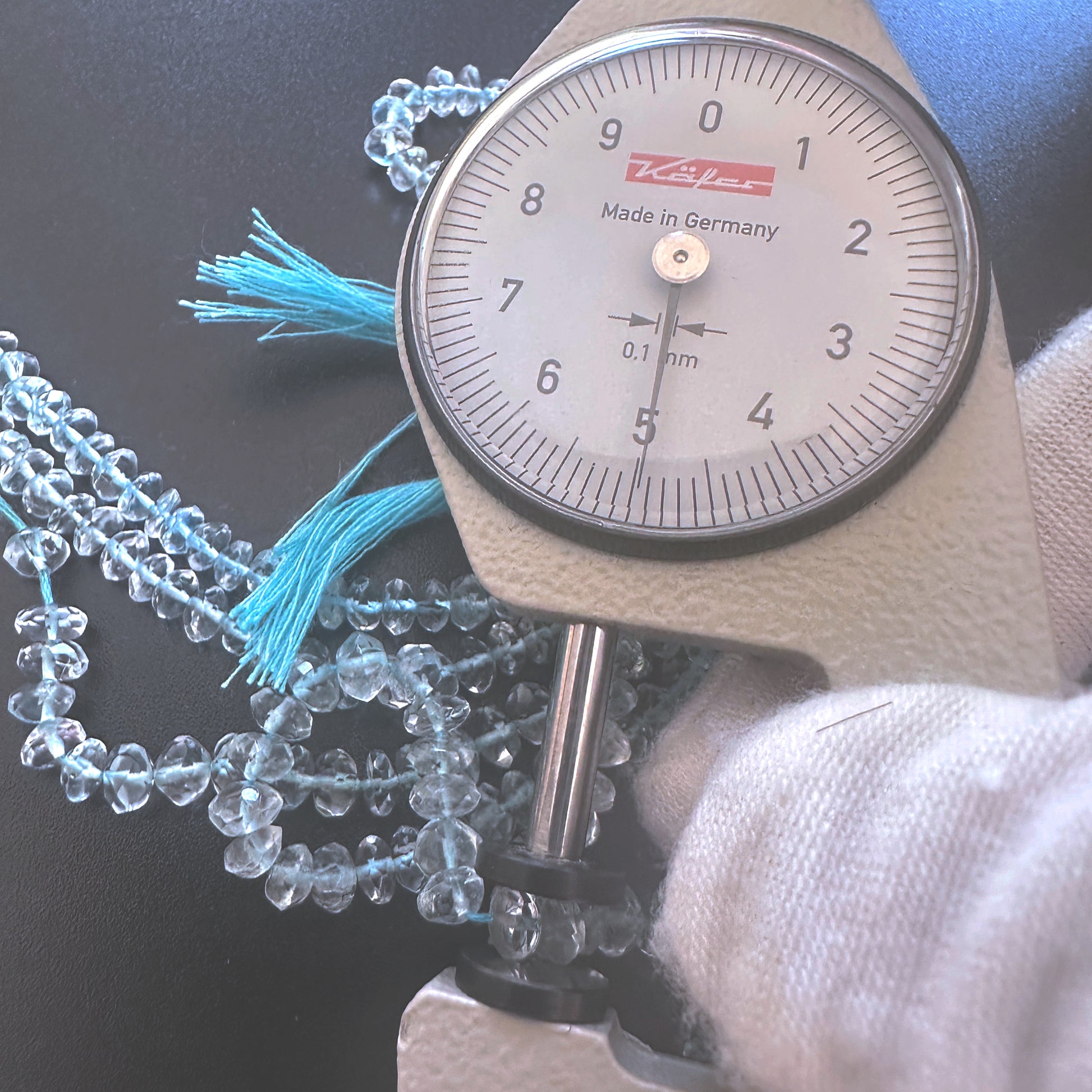 A dial gauge measures the aquamarine faceted rondelle  gemstone for accuracy.