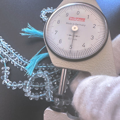 A dial gauge measures the aquamarine faceted rondelle  gemstone for accuracy.