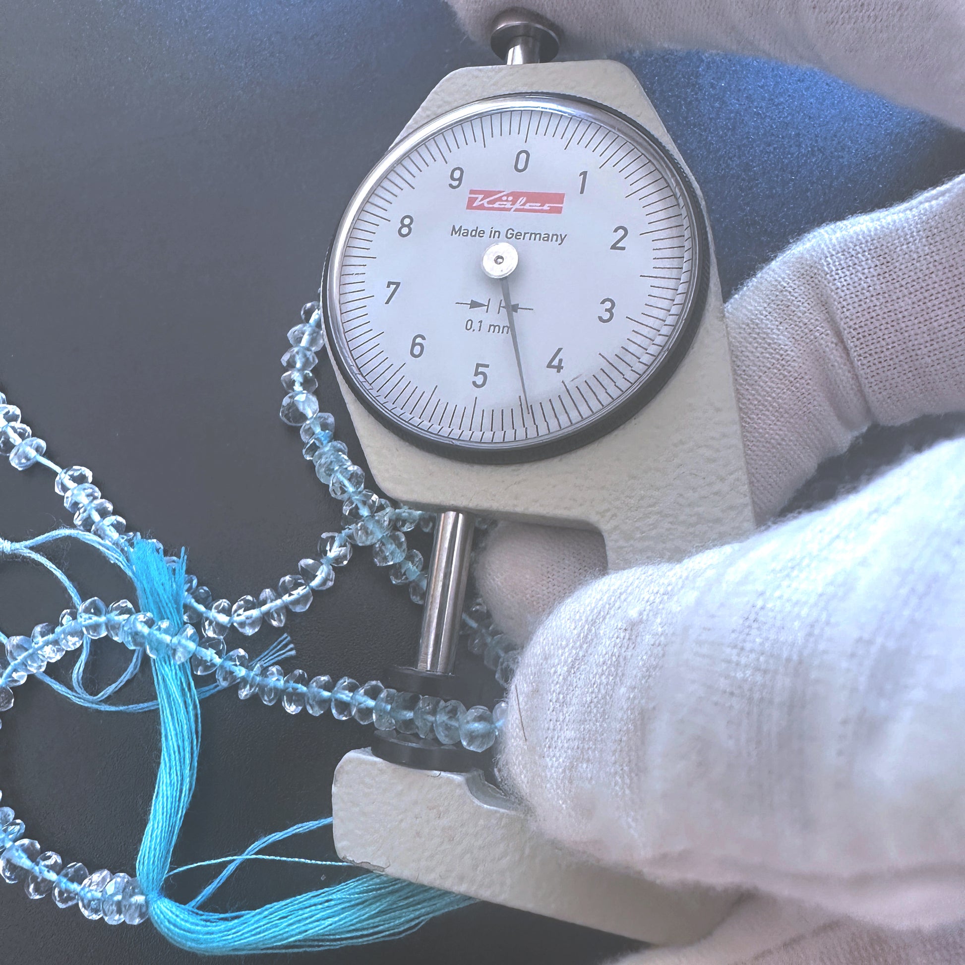 A dial gauge measures the aquamarine faceted rondelle  gemstone for accuracy.