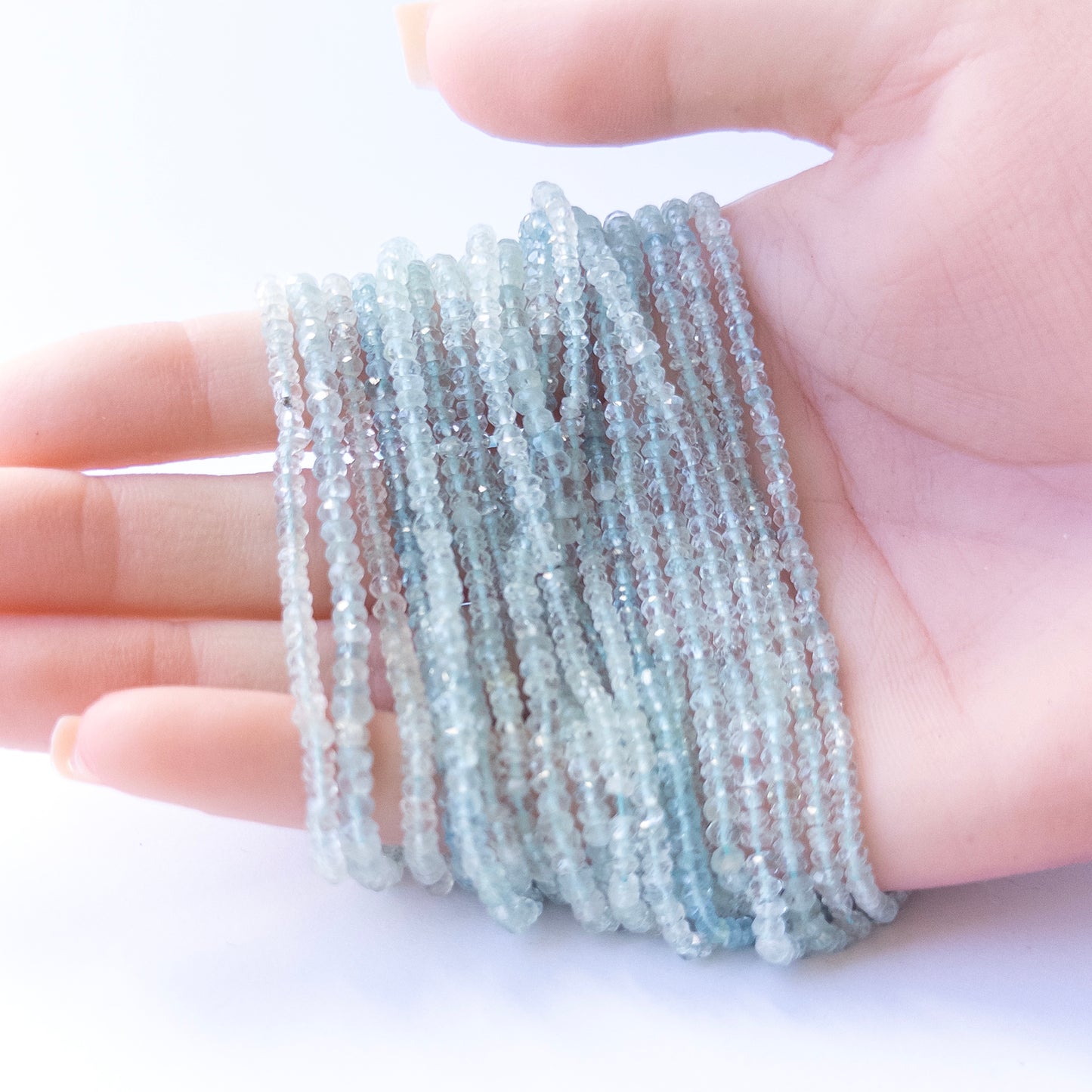 A person holds delicate strands of Aquamarine beads, showcasing their faceted rondelle design.