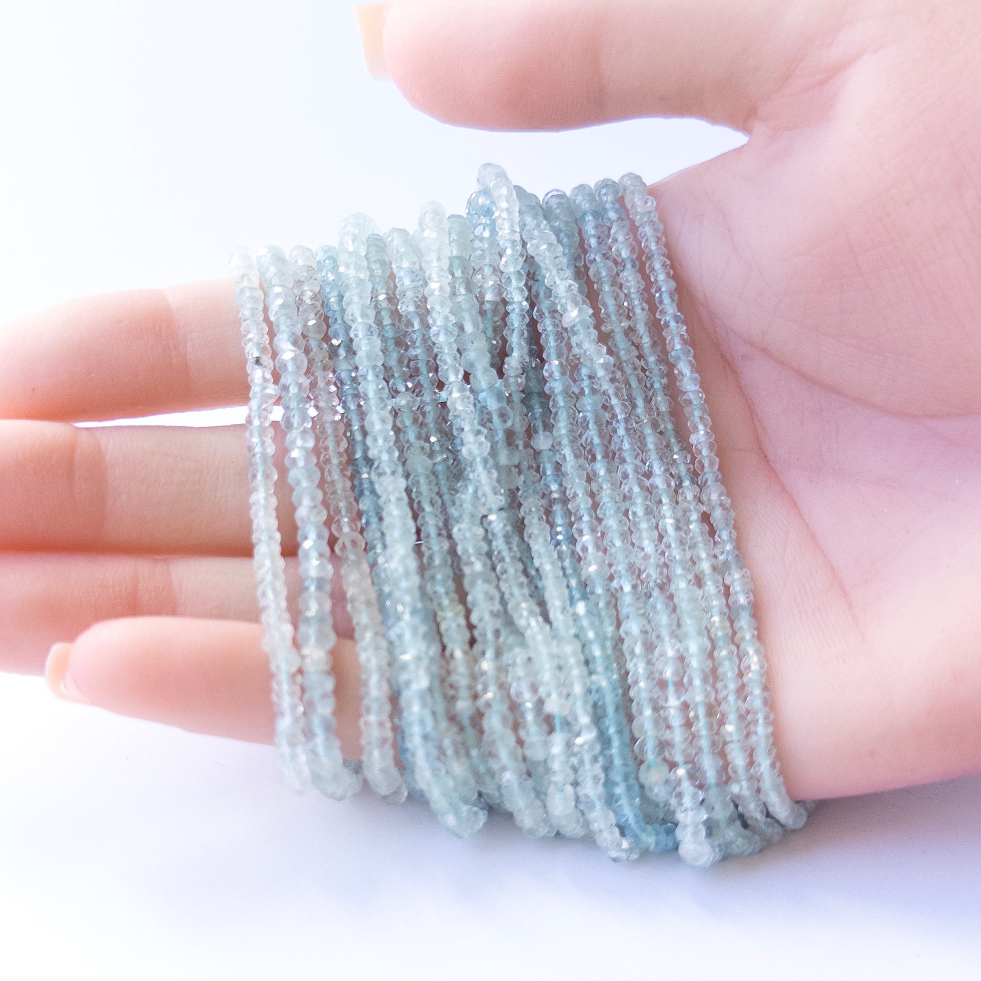 A person holds delicate strands of Aquamarine beads, showcasing their faceted rondelle design.