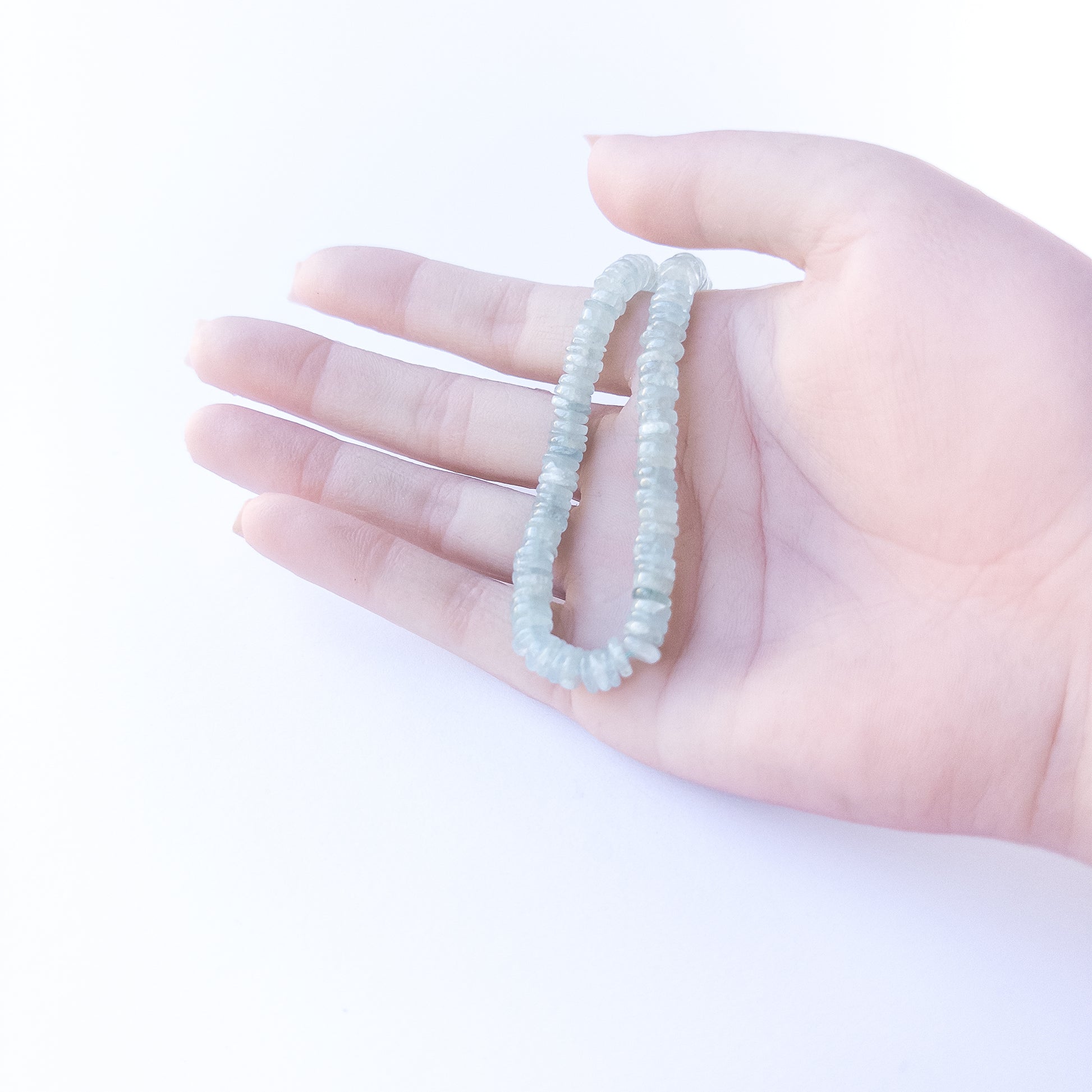 A person holds delicate strands of Aquamarine beads, showcasing their smooth wheel design.