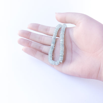 A person holds delicate strands of Aquamarine beads, showcasing their smooth wheel design.